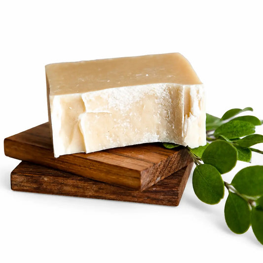 Bar of soap on a wooden soap dish with green leaves on a white background
