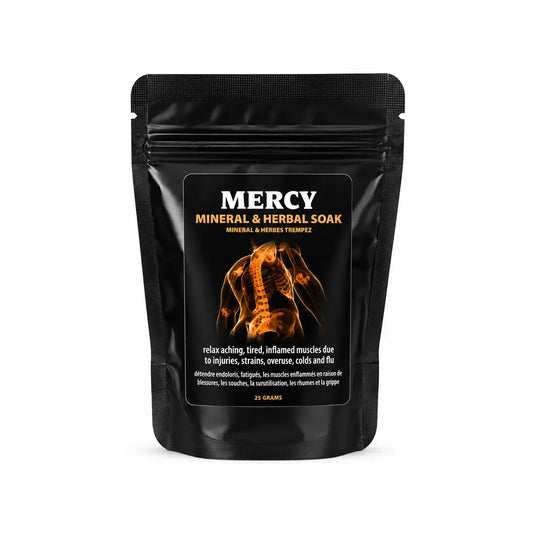A black stand-up pouch of Mercy Mineral & Herbal Soak on a clean white background. The front label features the brand name 'MERCY' in white, product details in gold and white, and an orange graphic of a human spine.