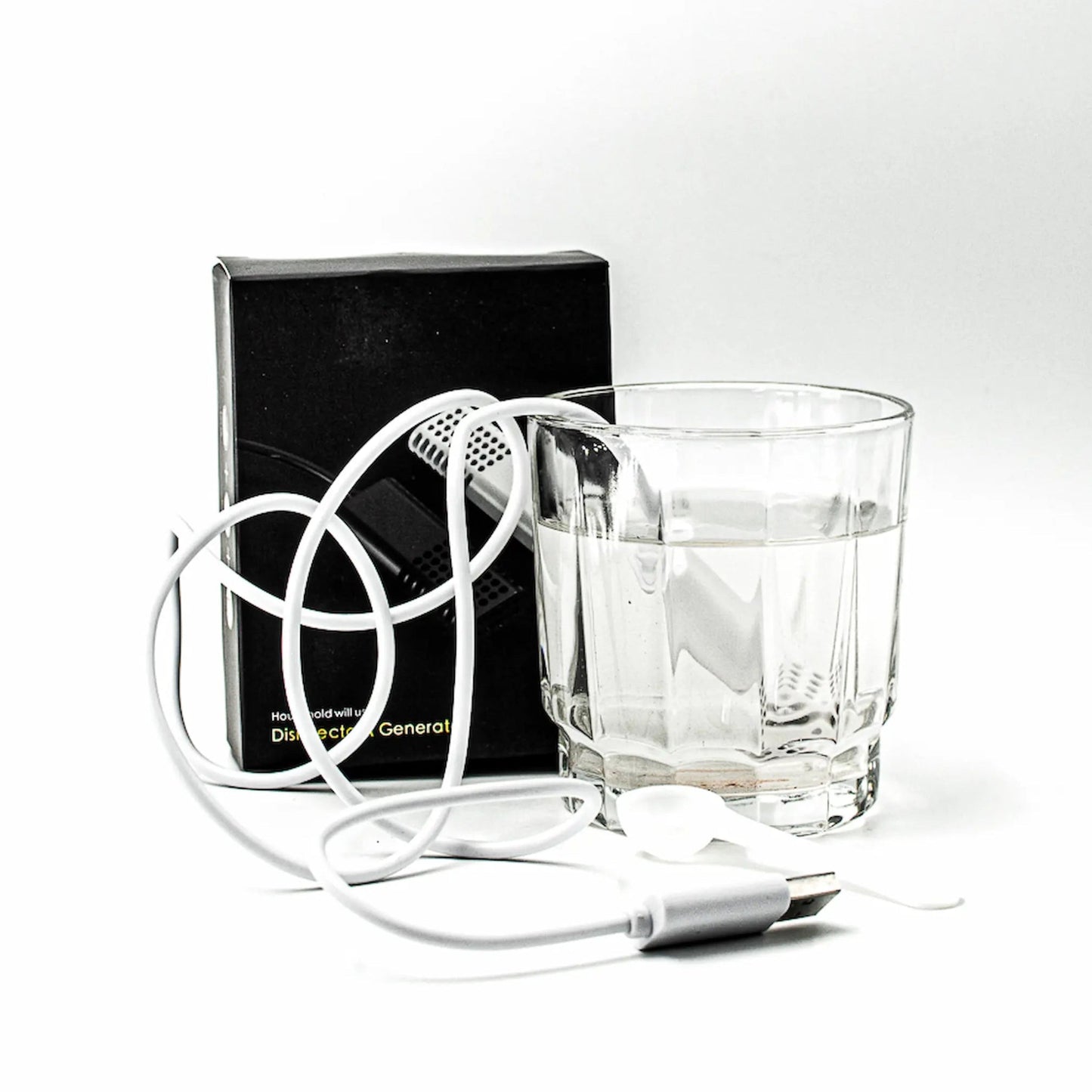 A white portable hypochlorous acid maker is shown with its black retail box, a clear glass of water, and a coiled white cord on a white background.